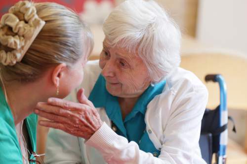 Caregiver and elderly woman sharing a warm, reassuring moment of connection