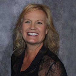 Sharon Scott smiling at the camera wearing black. Grey background.